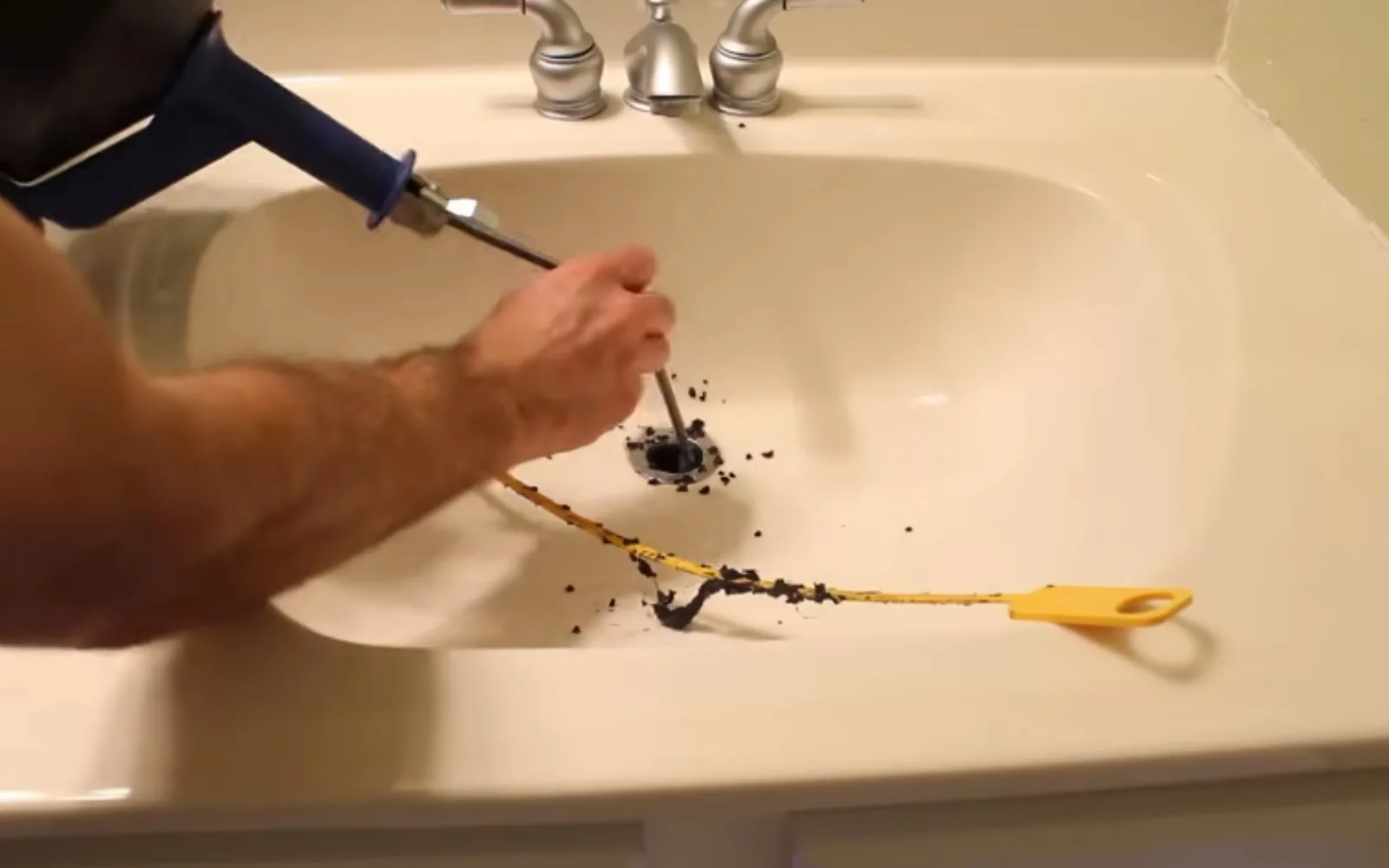Plumber using a drain snake to clear a clogged sink line