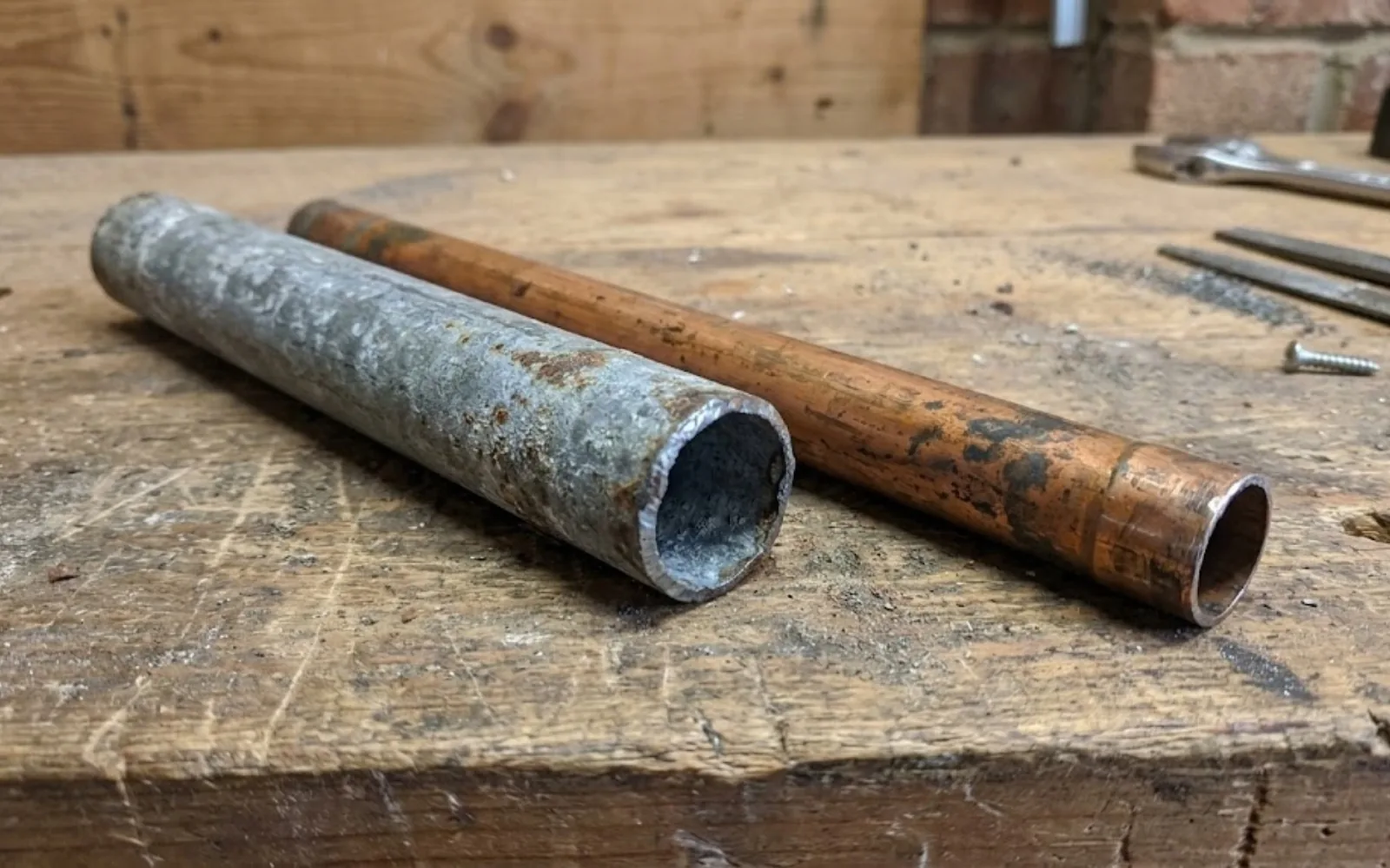 Galvanized steel pipe next to copper pipe, showing the dull gray versus reddish-brown color difference